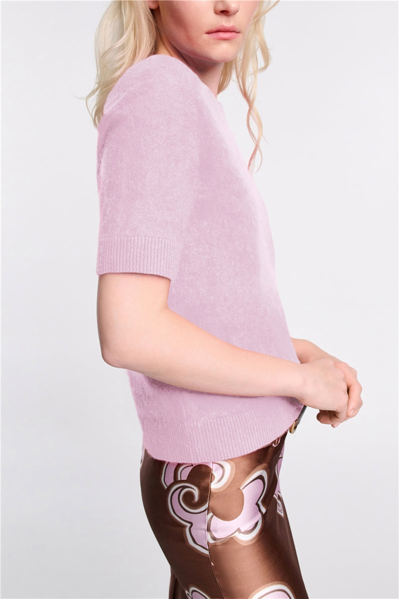 A person wears the Dorothee Schumacher Fluffy Statements Pullover in light pink with short sleeves and a brown patterned skirt, standing against a plain white background.