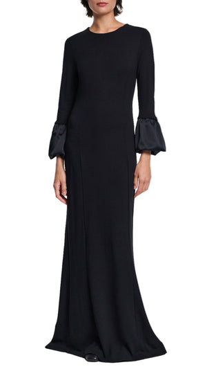 A woman wears the Dorothee Schumacher Cloudy Allure Dress, a long black midi made from wrinkle-free travel jersey with satin bubble cuffs, posed against a white background.