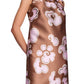 A person wears the Dorothee Schumacher Floral Statement Dress, a sleeveless brown satin shift featuring pink and white abstract floral patterns and a bow at the neckline.