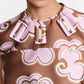A woman wears the Dorothee Schumacher Floral Statement Dress featuring a brown and pink key print and three rectangular jeweled embellishments near the neckline.