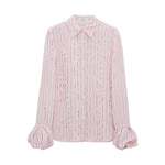 The Striped Ease Blouse by Dorothee Schumacher features light pink organdy voile with vertical black and white stripes, a pointed collar, and ruffled balloon cuffs, shown on a plain white background.