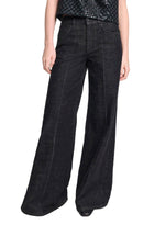 Model wears the Deep Love Pants by Dorothee Schumacher—wide-leg, dark wash black jeans—paired with a textured black top, set against a white background.