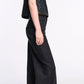 A woman stands in profile against a white background, wearing dark wash, wide leg Deep Love Pants by Dorothee Schumacher and a sleeveless black textured top for a modern, chic look.