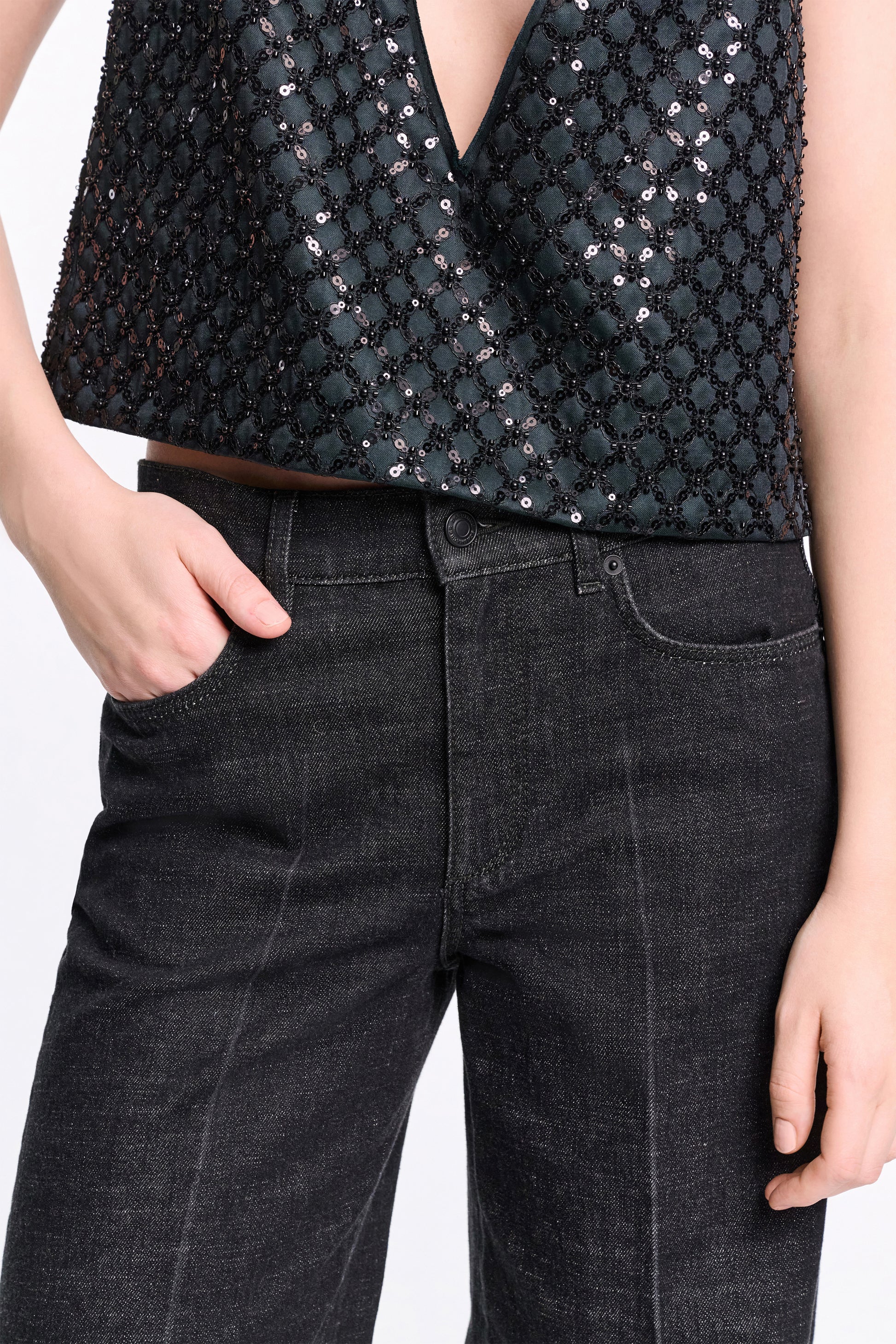 Model wears Dorothee Schumacher’s Deep Love Pants—dark wash, wide-leg, mid-rise jeans—paired with a dark sequined sleeveless top, one hand in the pocket and the other by their side.