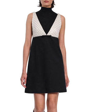 A woman wearing the Emotional Essence Dress by Dorothee Schumacher—a sleeveless black Punto Milano dress with a high neck, deep V-neckline white textured bodice, and a small waist bow.