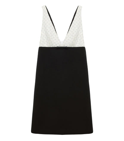 The Emotional Essence Dress by Dorothee Schumacher features a sleeveless V-neck, a white textured bodice, solid black skirt, and a small black bow at the waist.