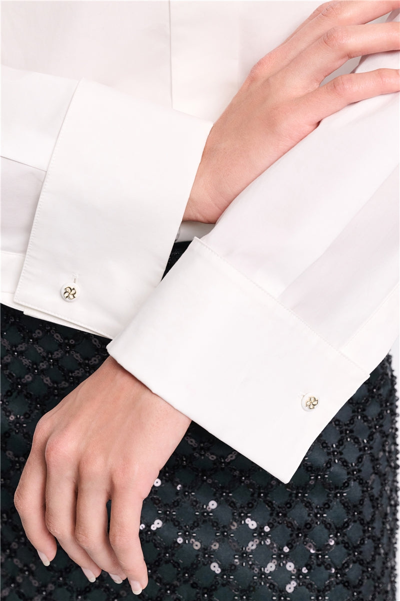 A person wearing the Dorothee Schumacher Poplin Power Bow Blouse paired with a black skirt featuring sequin floral embroidery.