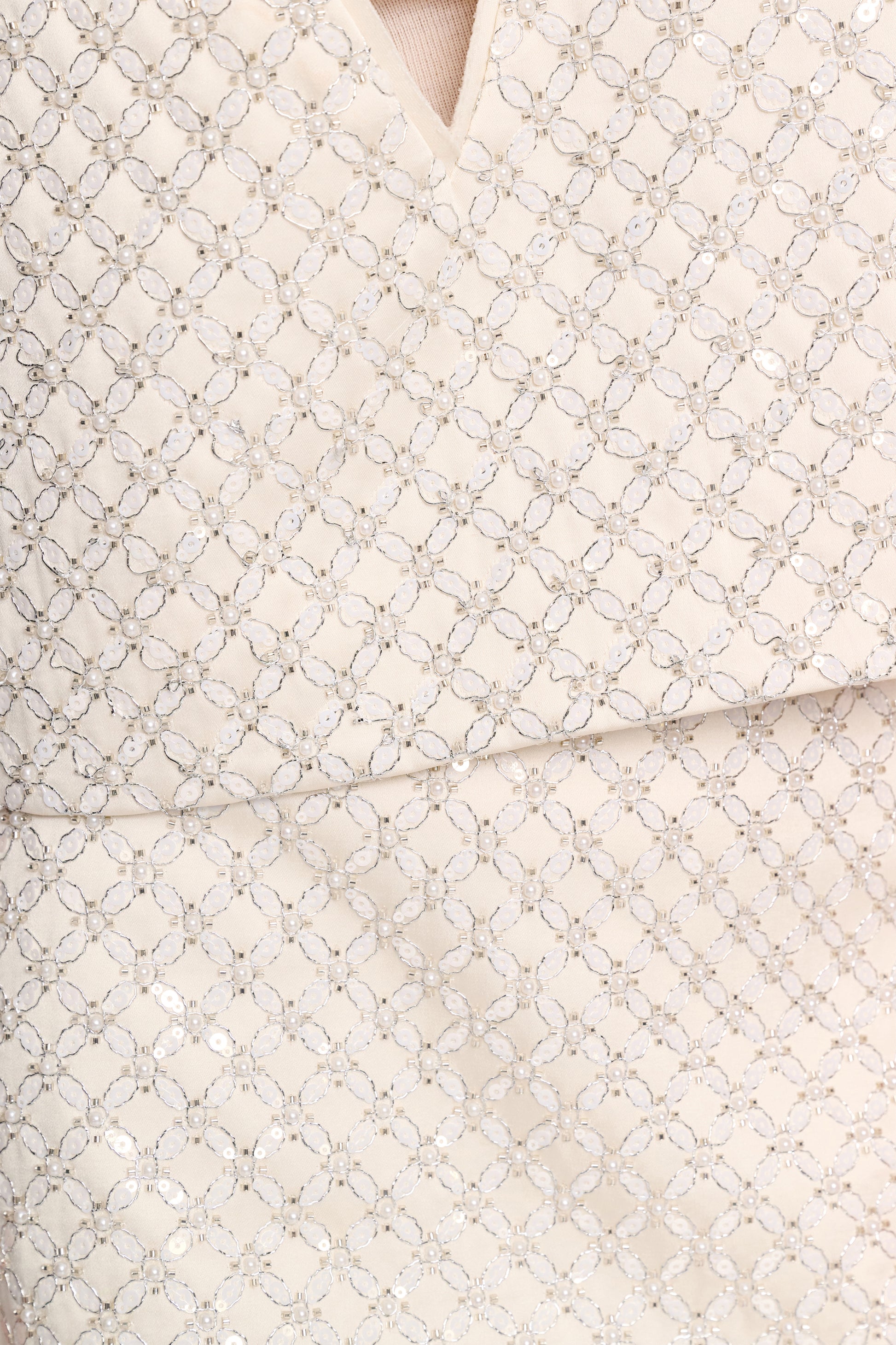 Close-up of light beige fabric with a diamond and circle embroidered pattern, featuring a seam and V-neckline—perfect for styling with the Dorothee Schumacher Sparkling Statement Mini Skirt.