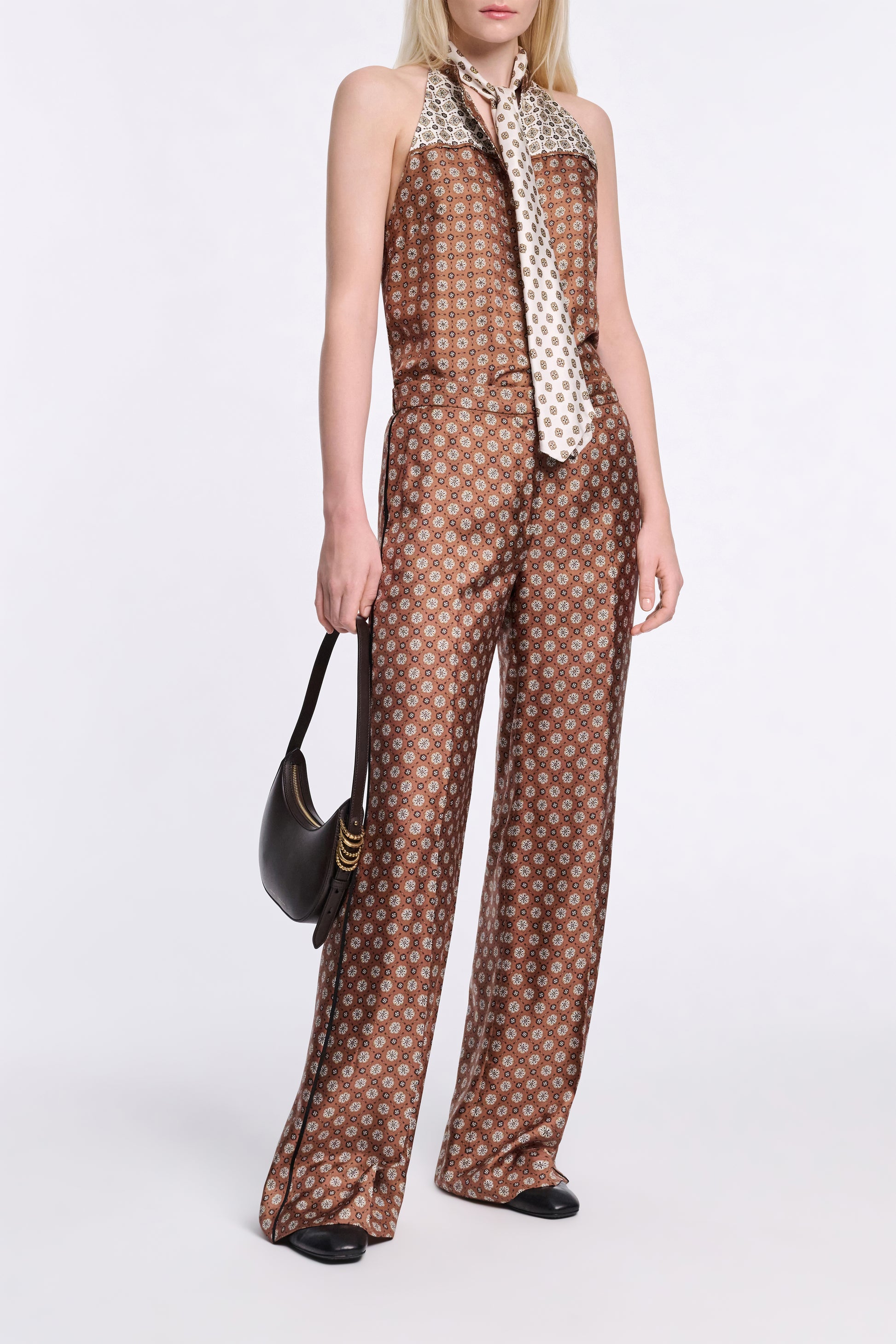 A person stands against a plain background wearing Dorothee Schumacher's Graphic Dreams Pants with a signature print, paired with a contrasting necktie, black handbag, and black shoes.