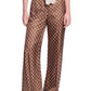 A person wearing Dorothee Schumacher's Graphic Dreams Pants—wide-leg, high-waisted brown signature print—with a matching sleeveless top and contrasting patterned tie.