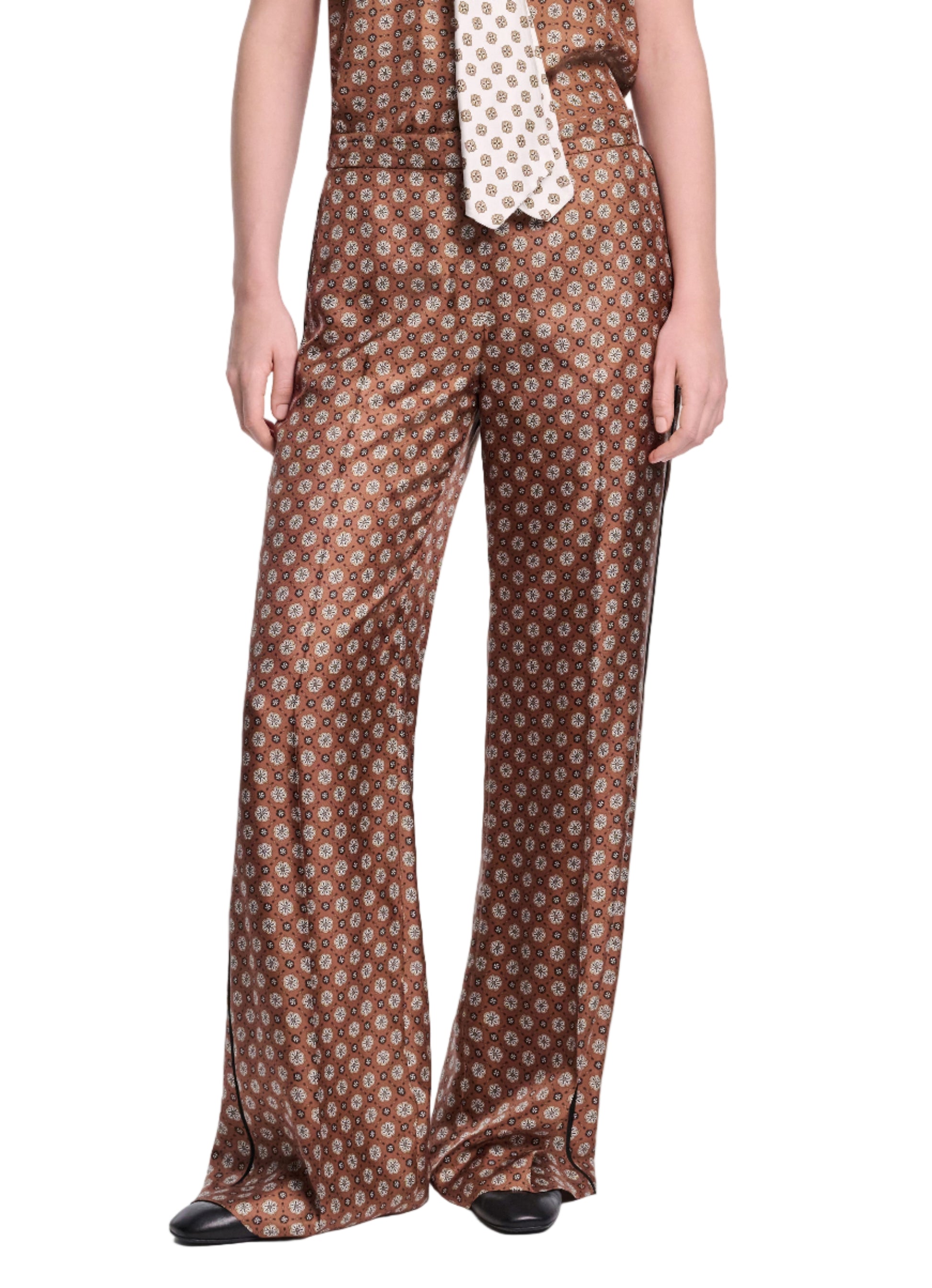 A person wearing Dorothee Schumacher's Graphic Dreams Pants—wide-leg, high-waisted brown signature print—with a matching sleeveless top and contrasting patterned tie.