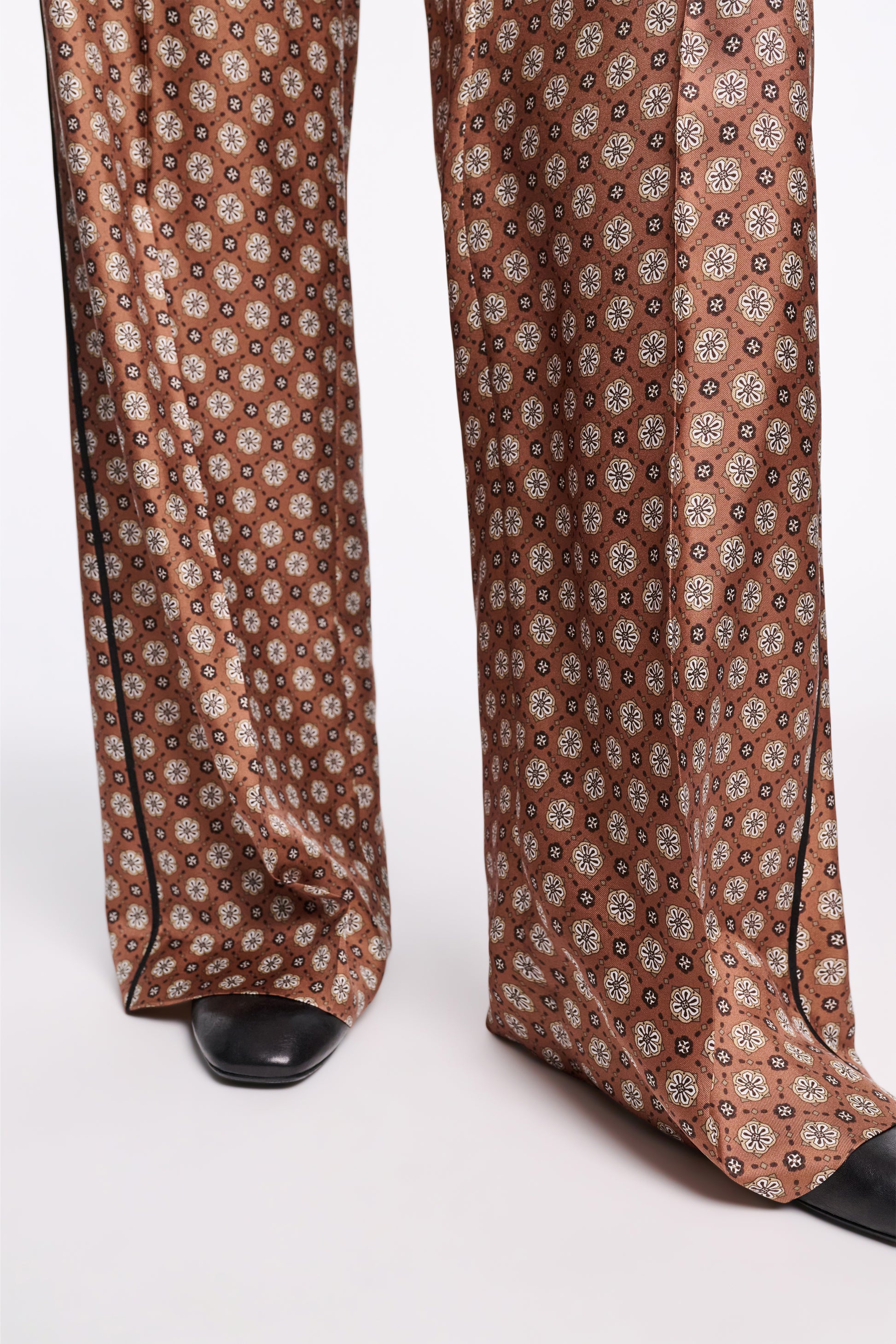 Close-up of a person wearing Dorothee Schumacher’s Graphic Dreams Pants in a signature print and wide-legged style, paired with black shoes on a white background.
