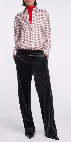 A person stands with hands in pockets against a plain background, dressed in the Dorothee Schumacher Graphic Dreams Blouse layered over a red turtleneck and loose black velvet pants.