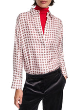 Person wearing the Dorothee Schumacher Graphic Dreams Blouse, a white patterned button-up, layered over a red turtleneck and styled with black pants. Hands are in pockets.