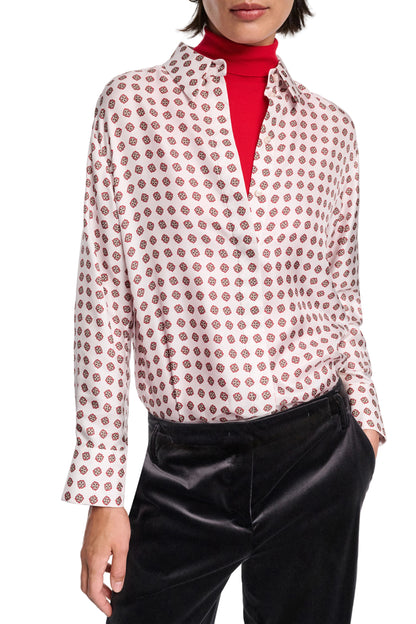 Person wearing the Dorothee Schumacher Graphic Dreams Blouse, a white patterned button-up, layered over a red turtleneck and styled with black pants. Hands are in pockets.