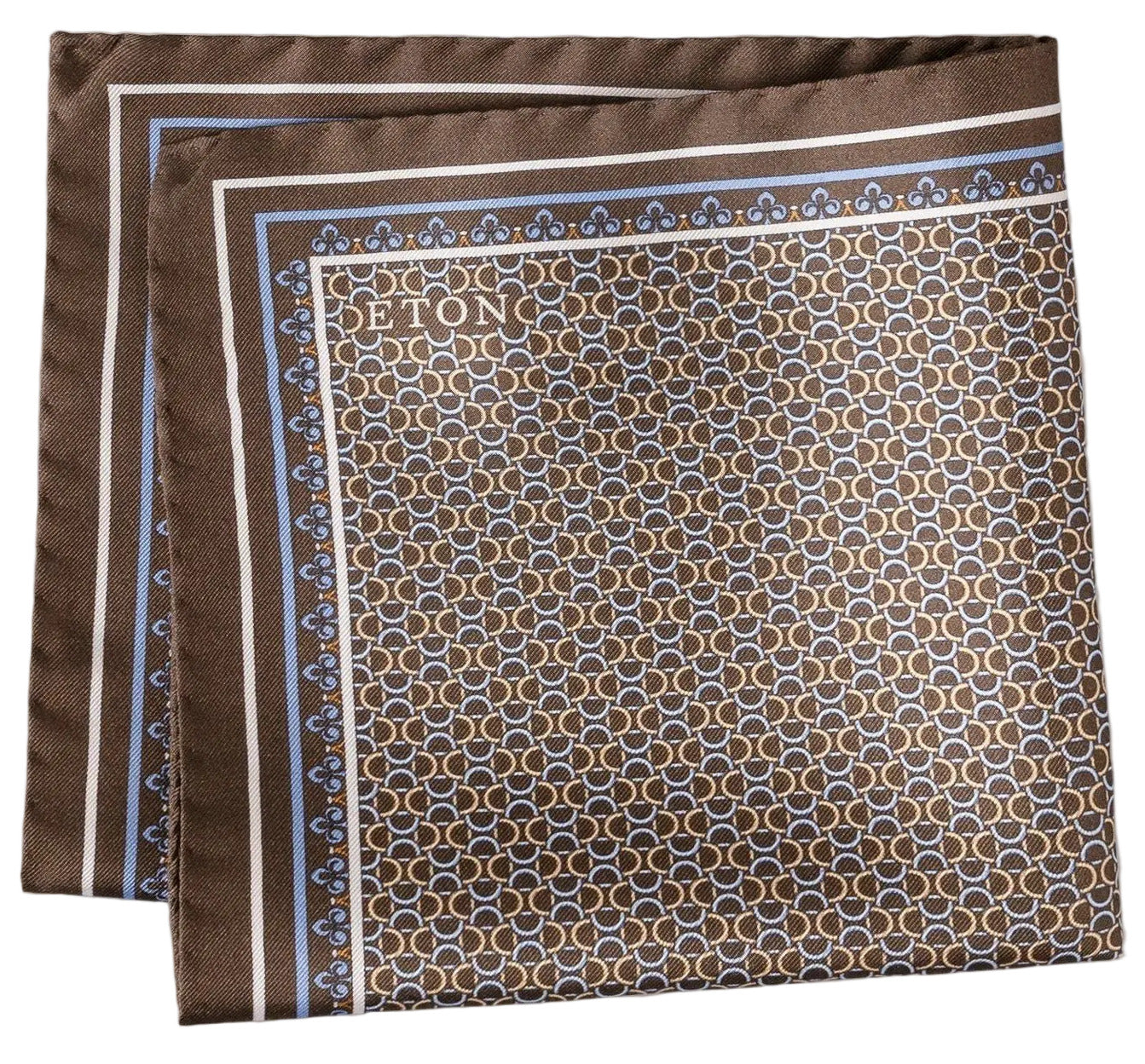 The Eton Geometric Silk Twill Pocket Square showcases a brown silk twill design with an Italian-printed blue and white hexagonal geometric pattern, a light blue border, and the "Eton" logo elegantly printed in one corner.
