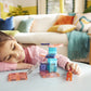 A young girl smiles as she enjoys creative hands-on play with the Magnatiles Cat Tree 13-Piece Set, building and exploring with magnetic pieces and an orange cat figurine in a colorful living room.