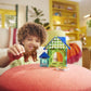 A child plays with the MagnaTiles Dog House 13-Piece Set, featuring colorful pieces, on a red ottoman in a brightly lit living room.