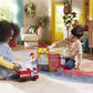 Two children sit on a colorful rug, engaging in imaginative play with building blocks, a toy fire truck, and the Magnatiles Fire Station 50-Piece Set in a sunlit living room decorated with plants.