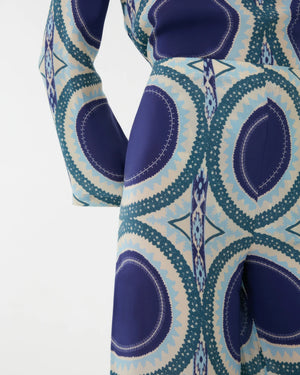 Close-up of a person wearing the Emporio Sirenuse Stephan Silk Solaris Pants, featuring blue, teal, and cream circular geometric patterns on soft silk crêpe.