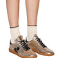 Legs flaunt cream socks and the chic Kaycee Sneaker in light gold metallic leather by Isabel Marant, featuring black laces, a black circular design, and a fashionable gum sole.