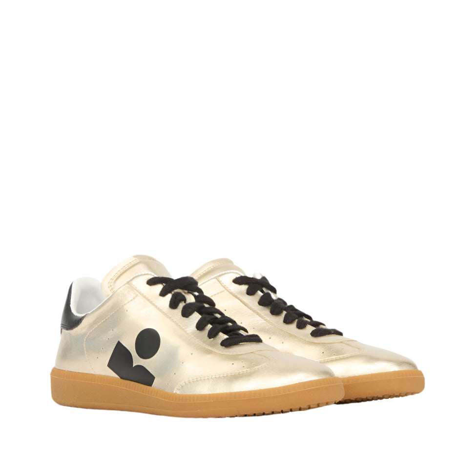 The Isabel Marant Kaycee Sneaker boasts light gold metallic leather, black laces and logo, a white interior, and gum soles. Its chic design is evident from both the side and front angles.