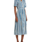 A person wearing the Emporio Sirenuse Claudia Ikat Stripe Dress, featuring a blue and white vertical stripe pattern with an Ikat Stripes collar and short sleeves, paired with brown sandals.