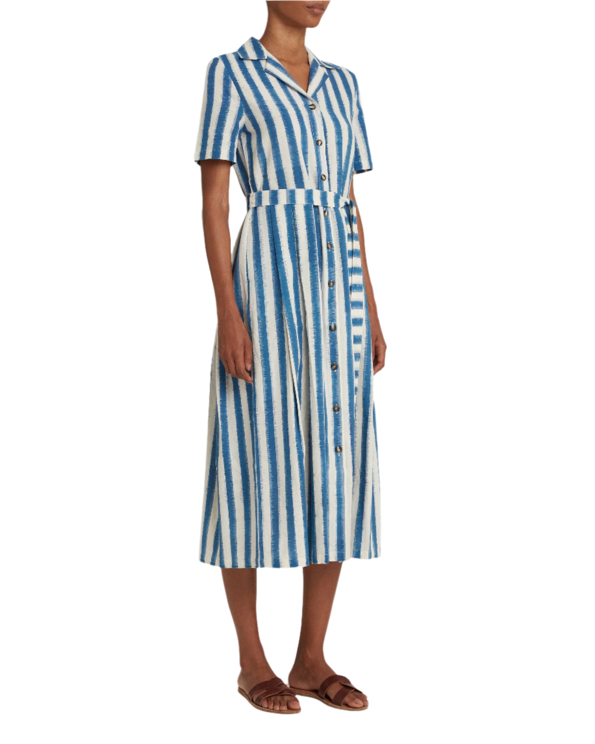 A person wearing the Emporio Sirenuse Claudia Ikat Stripe Dress, featuring a blue and white vertical stripe pattern with an Ikat Stripes collar and short sleeves, paired with brown sandals.