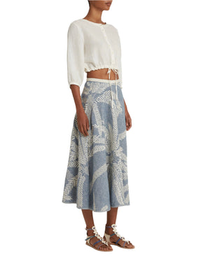 A person in a white cropped top and blue and white Emporio Sirenuse Tasha Palm Embroidery Skirt stands in sandals against a white background.