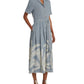 An individual wears an Emporio Sirenuse Claudia Palm Embroidery Dress in blue with fern patterns on the hem, made from elegant Japanese linen, paired with white sandals.