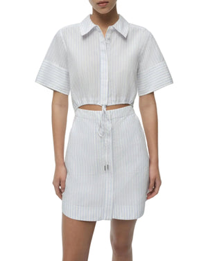 A woman wears the Simkhai Marcy Cotton Mini Shirt Dress, a short-sleeve, button-up style with light blue and white stripes, a drawstring waist, and a midriff cutout.