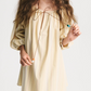 A woman with long, wavy hair wears the Bernadette Bonnie Short Stripe Dress—a loose summer style with puffed sleeves and a tie neckline—holding the ties in both hands.