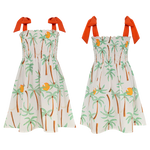 Two sleeveless Pepita & Me Girls' Waffle Dresses with orange shoulder ties feature a tropical palm tree and fruit print on white. The smocked top adds comfort and style—perfect for sunny days. Made in Colombia.