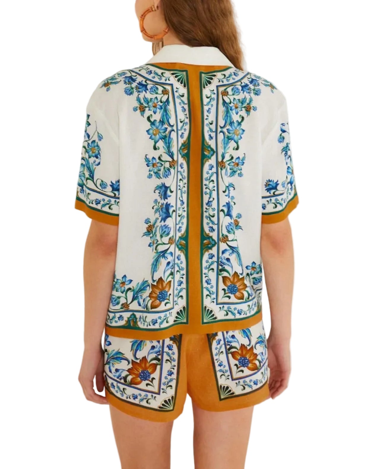 A woman stands with her back to the camera, wearing a Farm Rio Flora Tile Off White Blouse and matching shorts adorned with blue, green, and gold floral patterns.