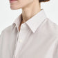 A woman shown from the shoulders up in side profile wears the Maria McManus Button Sleeve Crop Shirt, a light, pinstriped top made from Japanese Supima cotton, paired with silver earrings against a plain background.