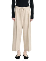 A person is wearing the Maria McManus Drawstring Trouser in beige wool-cashmere flannel with a wide-leg silhouette, styled with a black long-sleeve top and black flats, standing against a white background.