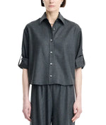 A person wearing the Maria McManus Button Sleeve Crop Shirt in dark gray wool flannel, featuring a cropped silhouette and rolled-up button sleeves, paired with matching wide-leg pants and standing against a plain white background.