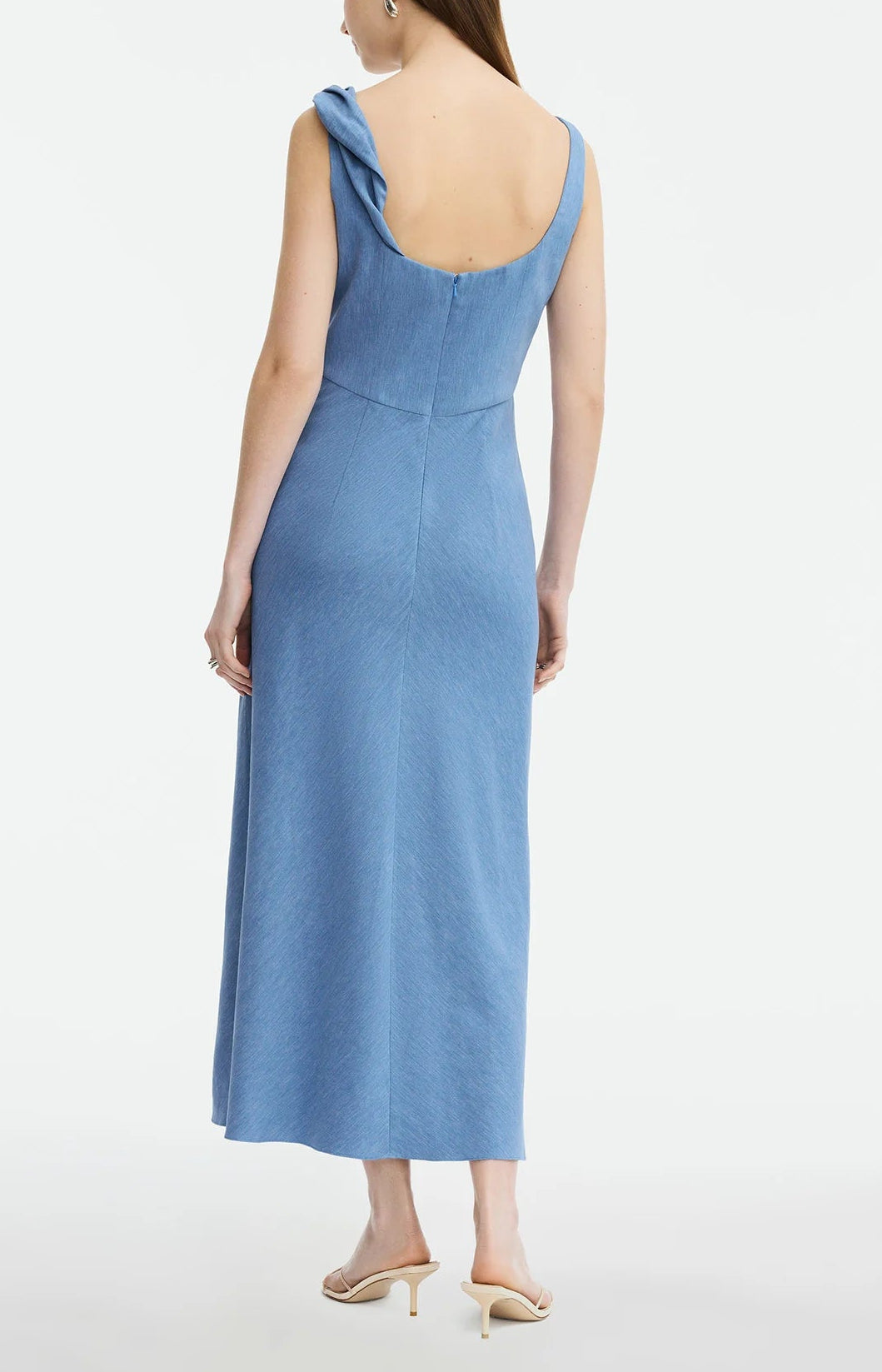 A model wears the Lela Rose Linen Twist Detail Dress—a sleeveless, light blue anti-wrinkle linen dress with a low back, side-zip closure, and A-line skirt—paired with heeled sandals against a plain white background.