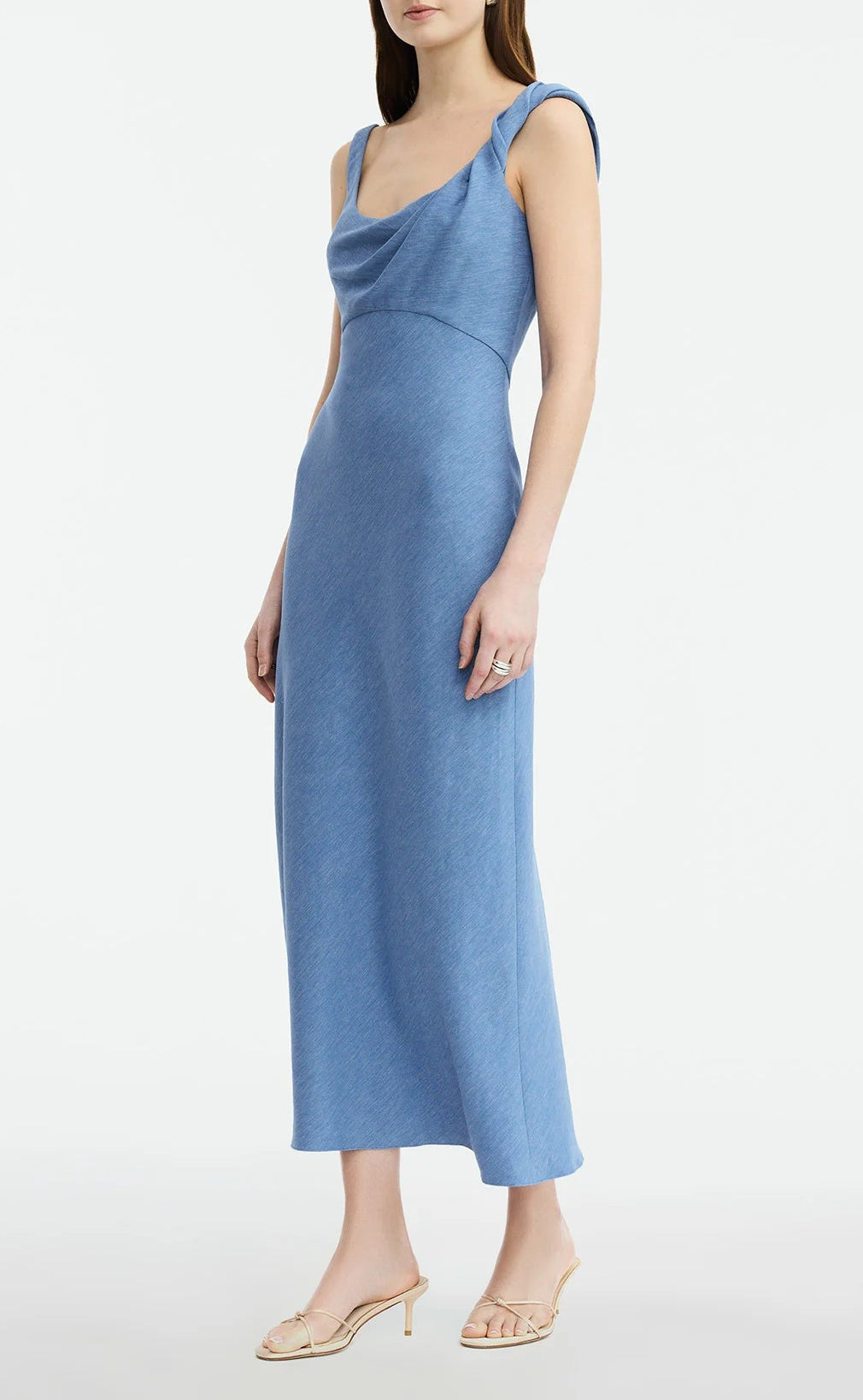 A woman models the Lela Rose Linen Twist Detail Dress—sleeveless, light blue, with an A-line skirt—paired with beige heeled sandals against a plain white background.