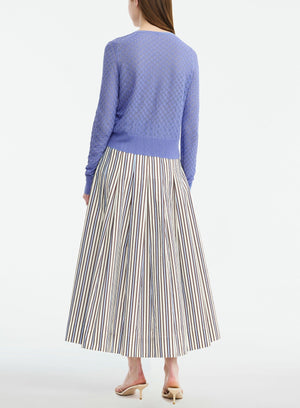 Back view of a person wearing a periwinkle blue Lela Rose Pointelle Knit Cardigan with a textured diamond pattern and a pleated, floor-length skirt featuring brown and blue vertical stripes.