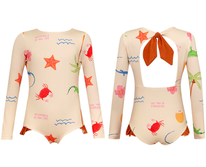 Two Pepita & Me Baby Girls' and Girls' Knot LS Rashguard swimsuits feature long sleeves, beige fabric with colorful sea-themed prints (crabs, starfish, plants), UPF50+ sun protection, and a back cutout with a large rust-colored bow.