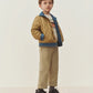 A young child stands facing forward against a plain off-white background, wearing the Bonpoint Boys’ Marvin Reversible Jacket with Embroidery on the Back, featuring denim trim, paired with beige pants, black shoes, and a graphic T-shirt.