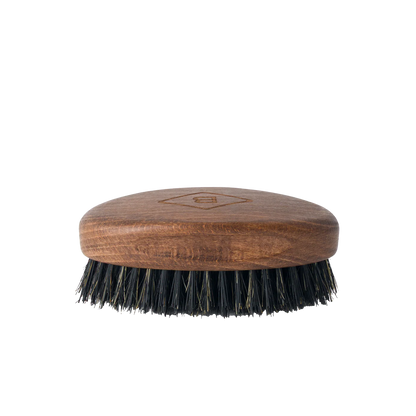 The Barberino's Beard Brush is a small oval brush with a wooden handle and dark natural bristles, ideal for grooming your beard. Shown against a plain white background.