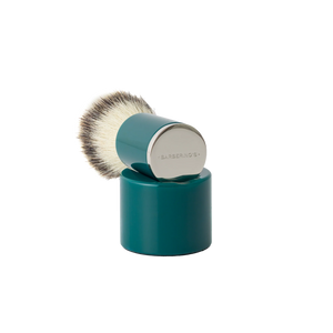 The Barberino's Cruelty Free Shaving Brush features a teal synthetic bristle brush with a cylindrical handle and silver cap, resting upright on a matching teal stand—ideal for a traditional shaving experience.