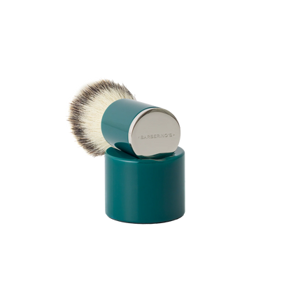 The Barberino's Cruelty Free Shaving Brush features a teal synthetic bristle brush with a cylindrical handle and silver cap, resting upright on a matching teal stand—ideal for a traditional shaving experience.
