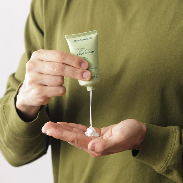 A person in a green shirt squeezes Barberino’s Ultra Hydrating Face Cream, ideal for men's skincare, from a green tube into their palm.