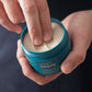 A person scoops Barberino's Matt Paste from a blue container with two fingers, ideal for creating textured hairstyles with a matte finish.
