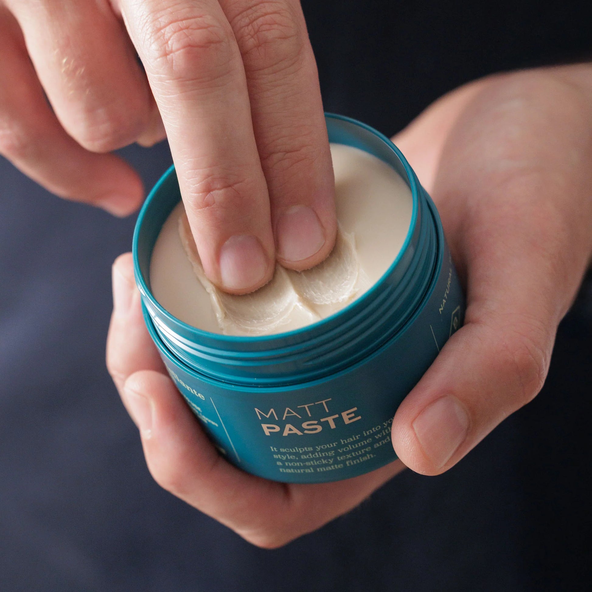 A person scoops Barberino's Matt Paste from a blue container with two fingers, ideal for creating textured hairstyles with a matte finish.