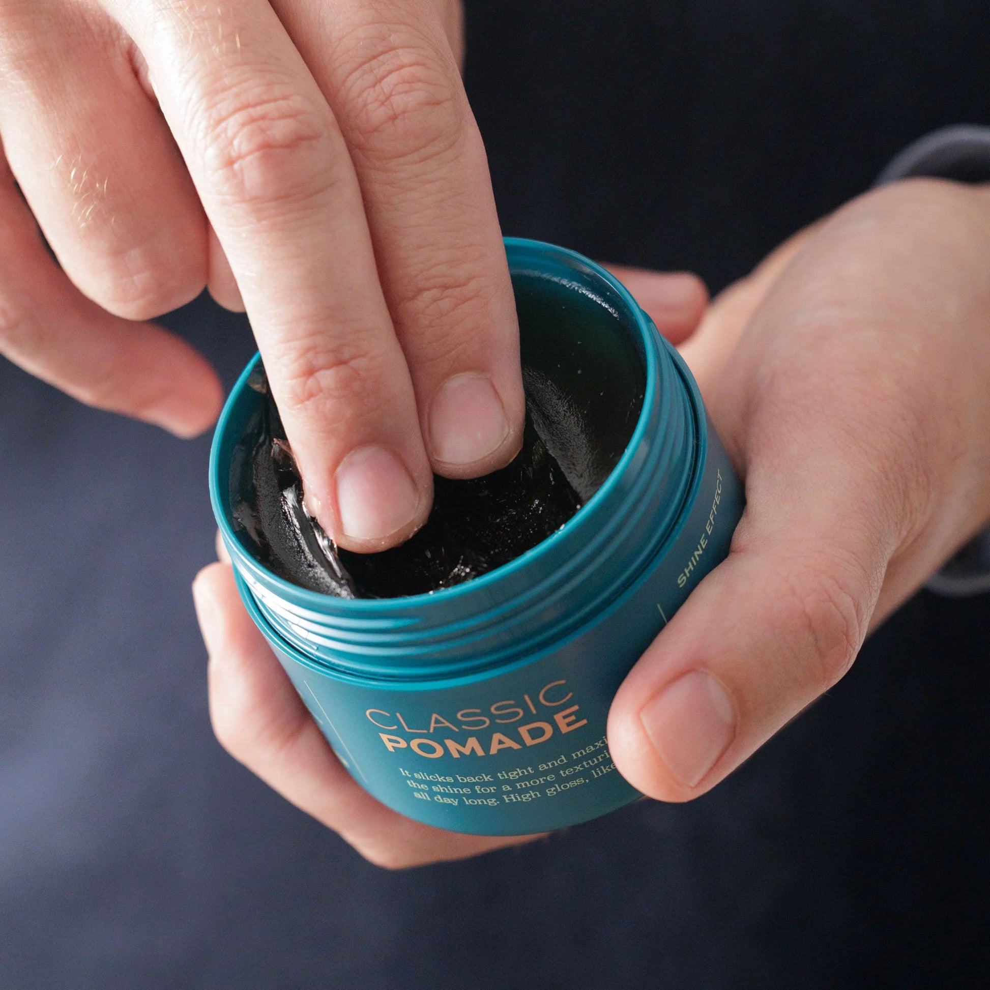 A person scoops medium-hold BRB Classic Pomade from Barberino's blue container, capturing timeless gentlemen’s grooming.