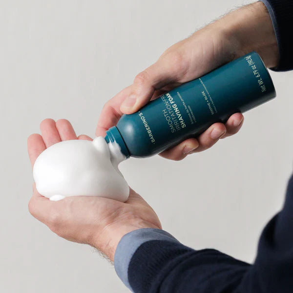 A person dispenses a generous amount of Barberino's Smooth Irritation-Free Shaving Foam from a blue canister into their palm, preparing for a comfortable shave.